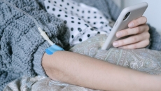 A person holding a phone with an IV in their arm