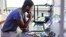 Worker looking at laptop surrounded by electronic components