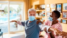 Patient in mask being examined in a home setting by healthcare worker in mask.