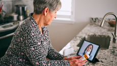 A woman looks at a medication bottle with a person onscreen.
