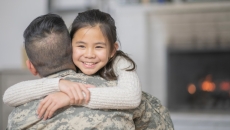 A person wearing military fatigues hugs a child.