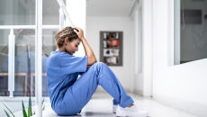 A clinician sits holding her head in a hallway
