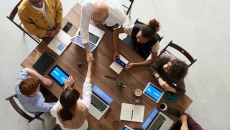 Top-down view of two cybersecurity specialists shaking hands as they sit across a table with others.