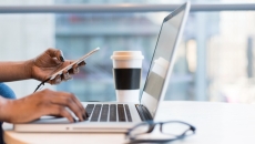 One hand rests on a laptop keyboard while the other holds a phone