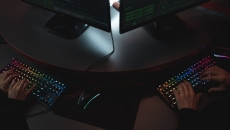 Two hackers type on keyboards in a shadowy room