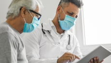 A doctor looks at a tablet with a patient looking over his shoulder