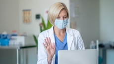 A doctor waves at a patient via telehealth