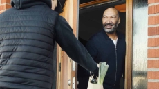 Individual delivers a bag of food to a person at the door of a brick building