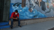 A person in a mask sits looking at their phone