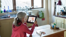 A person sits at a table speaking with a doctor via tablet.