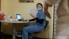 A person in scrubs and personal protective equipment sits at a computer