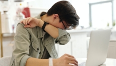 A person sneezes into their elbow in front of a computer