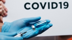 A person holding a syringe with the words "COVID19" on a sign in the background