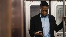 Man in shirt and blazer using his phone while standing in a subway car
