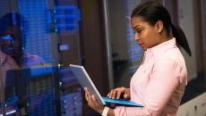 A person on a laptop in front of a server room
