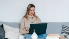 A person looking at a laptop while seated on a sofa.