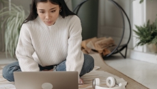 A laptop user in sweater and jeans sitting on the carpet