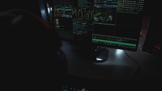 A shadowed figure views a computer terminal monitoring data streams.