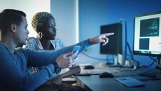Two people at a desk examine a screen