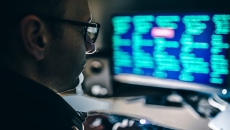 A person sits in a darkened room in front of a computer