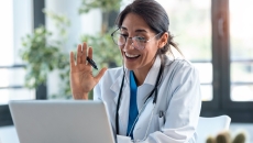 A doctor waves at a laptop screen
