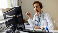 A doctor sits at a computer with a headset on