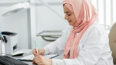 A nurse wearing hijab is filling out a patient form