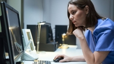 A nurse reading a medical record on a desktop computer