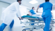 A doctor and healthcare workers race a patient on a gurney down a hospital corridor.