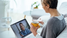 A patient holding a cup of coffee in a virtual consultation with a health professional