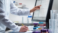 A lab researcher jotting down notes from a table flashed on a desktop computer
