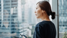 A person standing by a window using a smartphone.