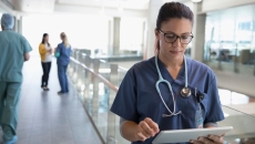 A doctor in a hallway reviewing a patient's file on a digital tablet 