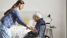 Nurse helps an elderly patient into a wheelchair at home