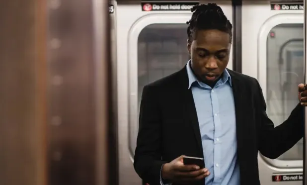 Man in shirt and blazer using his phone while standing in a subway car