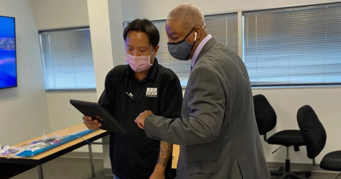 Two people stand with masks on looking at a tablet