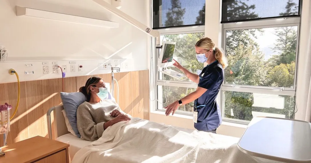 A nurse talking to a patient while using Rauland Australia's Concierge bedside terminal platform