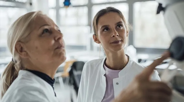 Two people in lab coats work with monitor