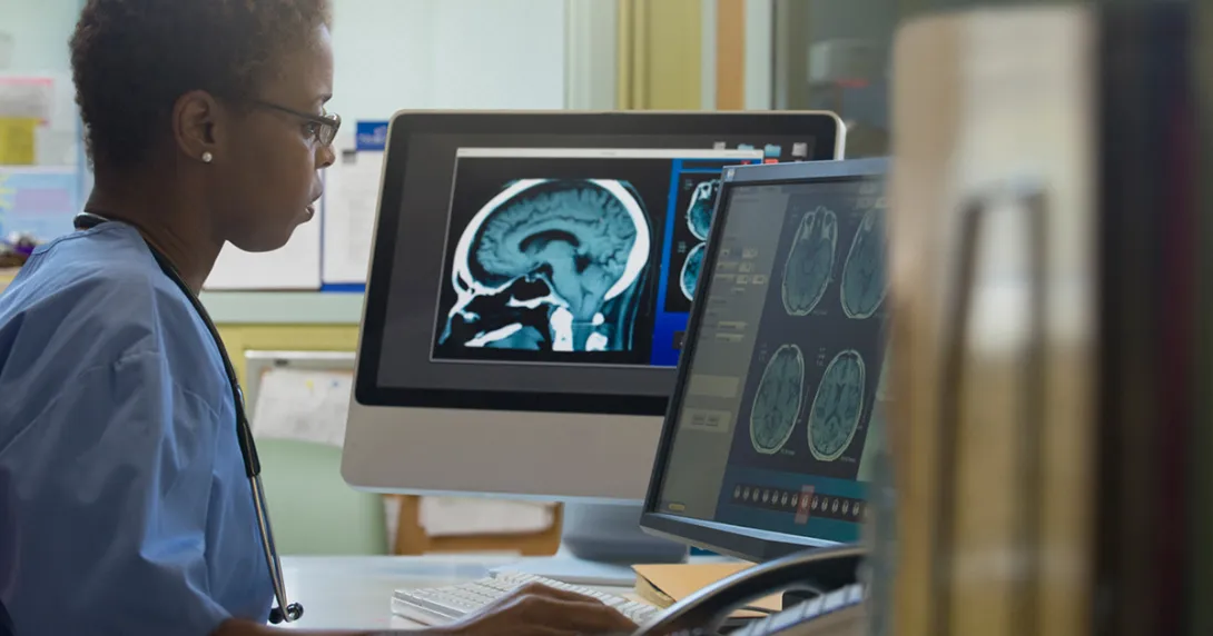 Healthcare worker with MRI image working on a computer Healthcare worker with MRI image working on a computer