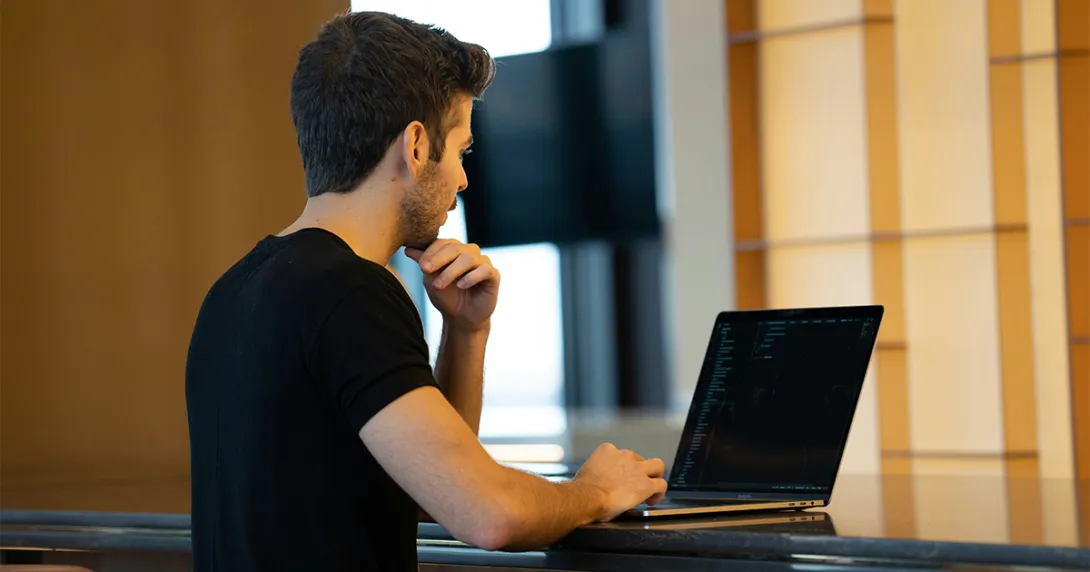 Man in black tshirt codes on a laptop Man in black tshirt codes on a laptop