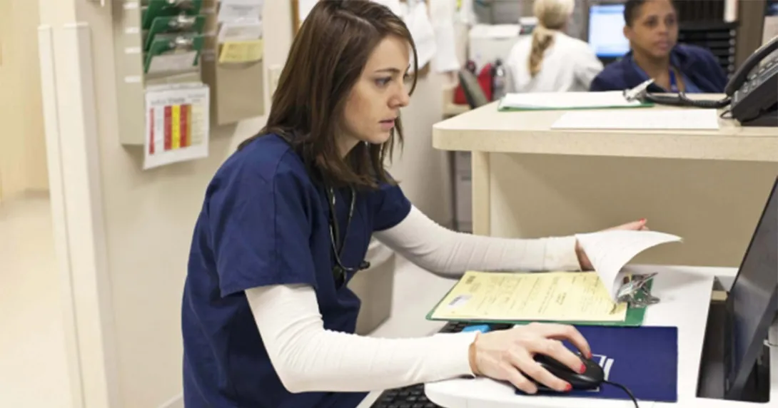 Nurse in scrubs sitting at a computer with notes Nurse in scrubs sitting at a computer with notes