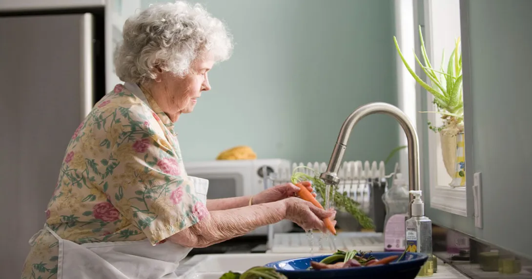 Woman with short hair washes carrots with an electric faucet. Woman with short hair washes carrots with an electric faucet.