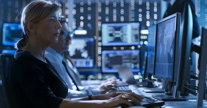 A person sits in a darkened room in front of a wall of computers