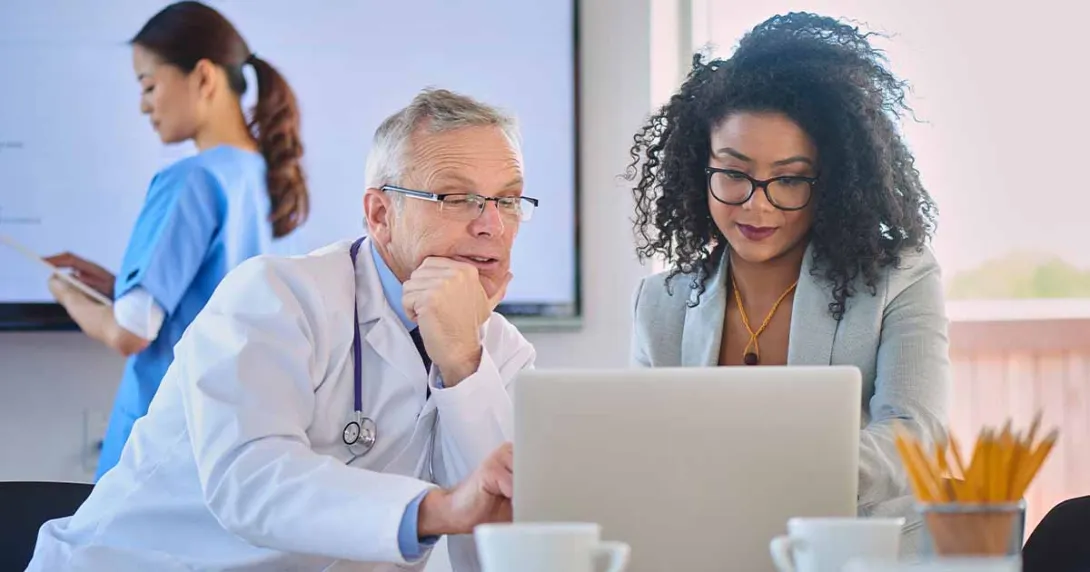 Doctor and businessperson looking at laptop screen Doctor and businessperson looking at laptop screen