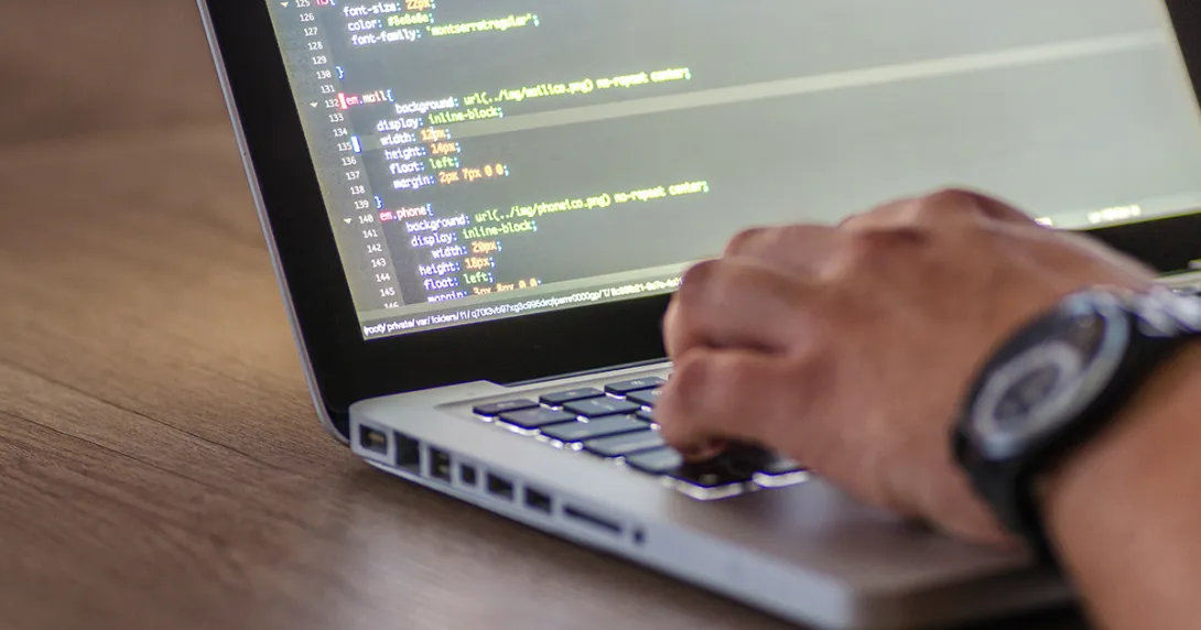 Close-up of a software developer's hand on a laptop with code on the screen Close-up of a software developer's hand on a laptop with code on the screen