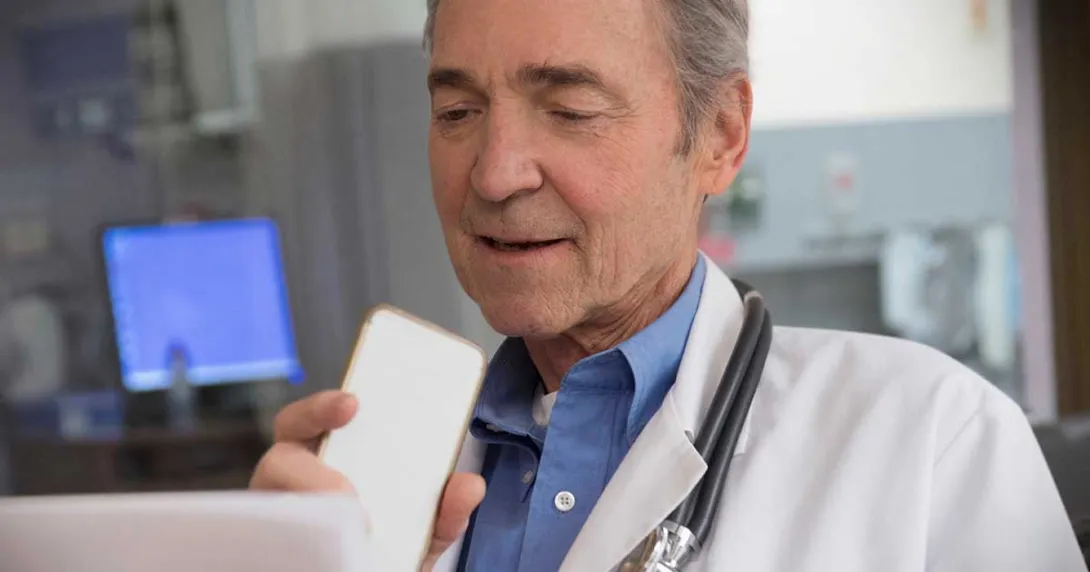 Gray-haired doctor sitting at a monitor and talking into a cell phone Gray-haired doctor sitting at a monitor and talking into a cell phone