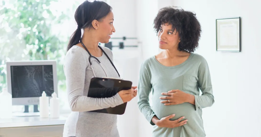 A doctor speaks with a pregnant woman, who puts her hands on her belly