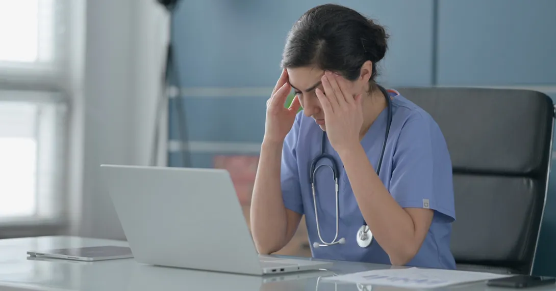 Nurse frustrated by documentation burden sitting in front of laptop Nurse sitting in front of laptop with hands to head