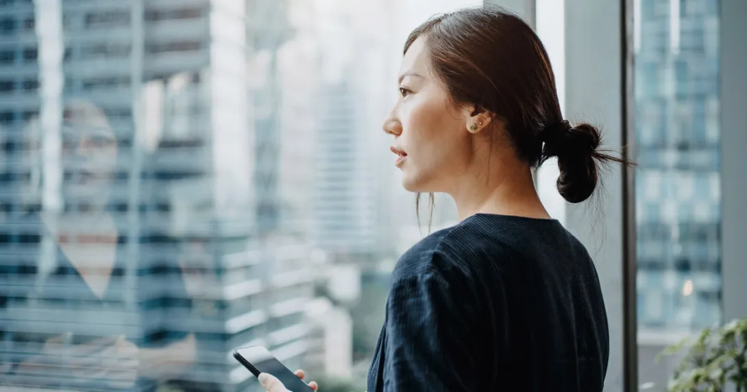 A person holding a smartphone looking out the window A person holding a smartphone looking out the window