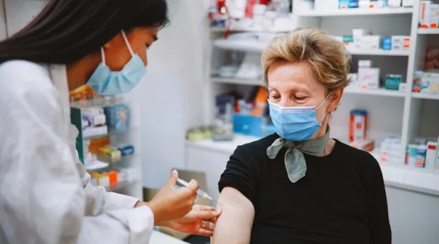 Healthcare worker in mask giving shot to patient in mask